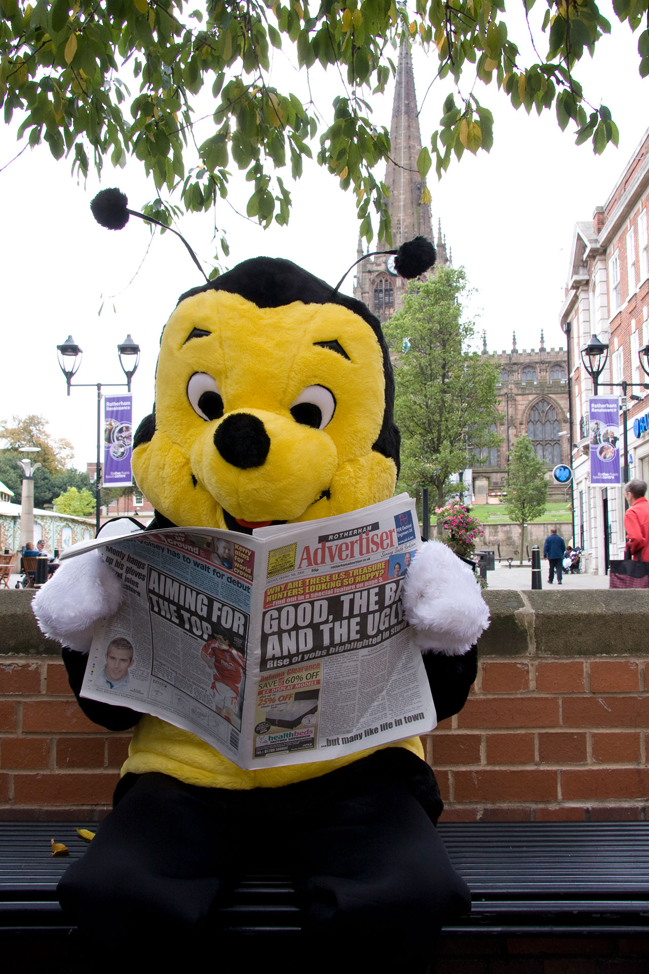 Human in bee costume reading a newspaper.
